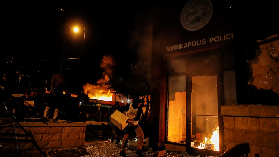 Un manifestant lance une caisse à l'intérieur d'un poste de police en feu en pleine nuit à Minneapolis.