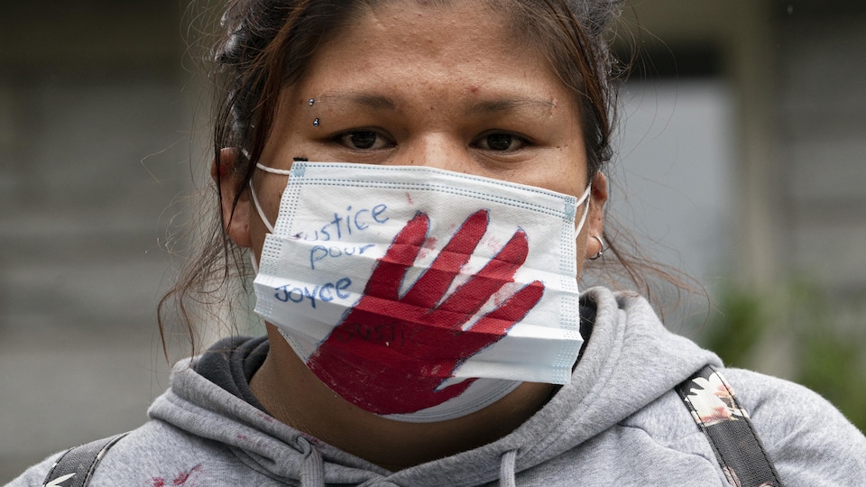 Une femme porte un masque où l'on peut lire : Justice pour Joyce.