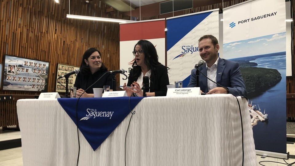 Trois personnes à une table lors d'une conférence de presse. 