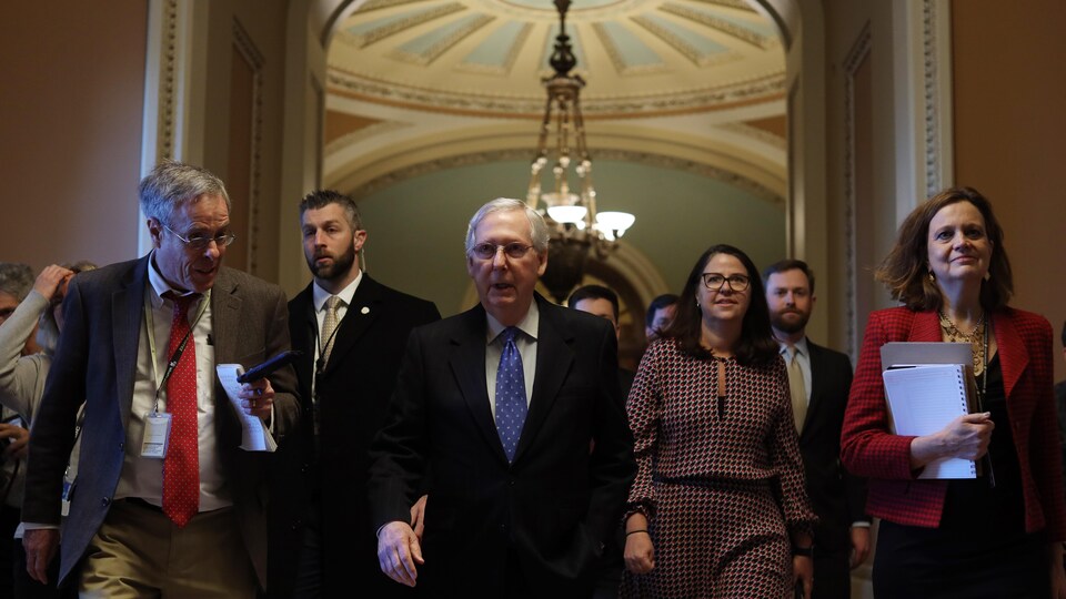 Mitch McConnell marche dans les corridors du Sénat entouré de ses collaborateurs.