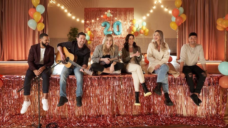 Les six personnes assises sur une table dans une salle décorée avec des ballons pour célébrer un 20e anniversaire.