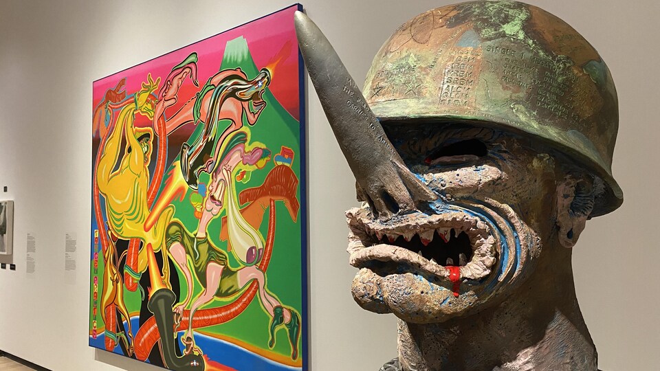 Une sculpture d'une tête de général d'armée portant un casque de guerre. Son nez est un missile. Derrière à gauche, un tableau coloré aux influences psychédéliques. 