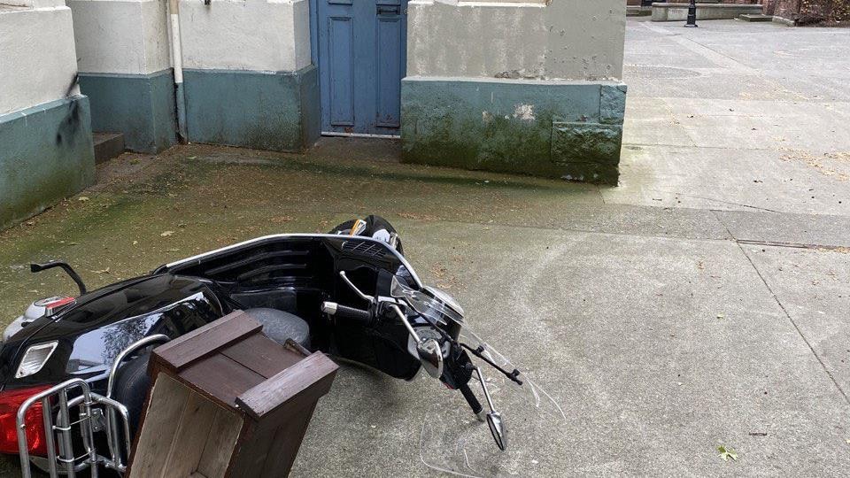 A moped overturned on the sidewalk, in front of a building.