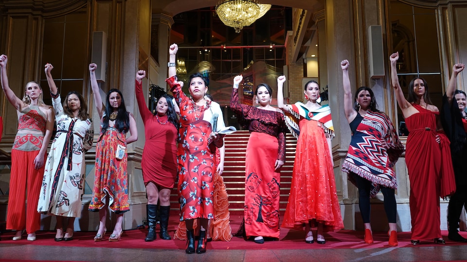 Une dizaine de femmes arborent des vêtements de couleur rouge et lèvent le poing droit.