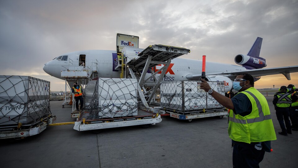 Des cargaisons devant un avion FedEx sur le tarmac d'un aéroport