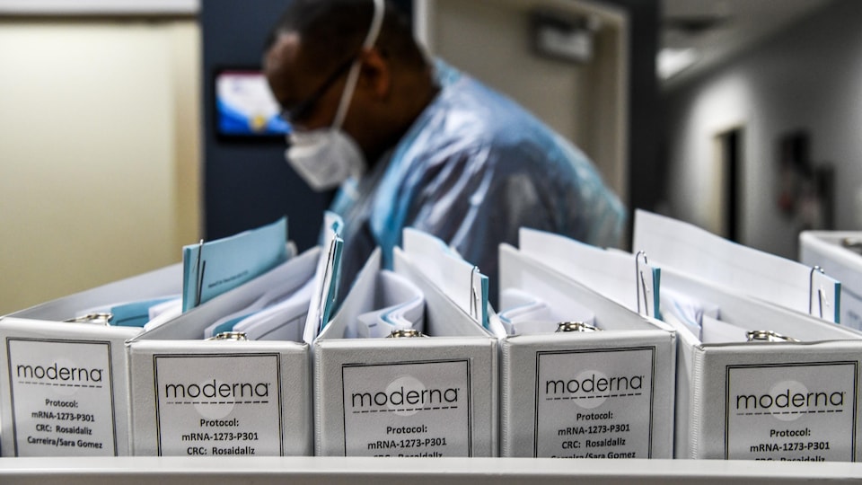 Un homme masqué, près des cartables contenant les protocoles pour le vaccin de Moderna.