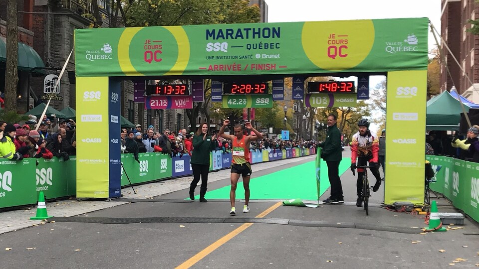 Mohamed Aagab lève les bras en franchissant le fil d'arrivée d'un marathon.