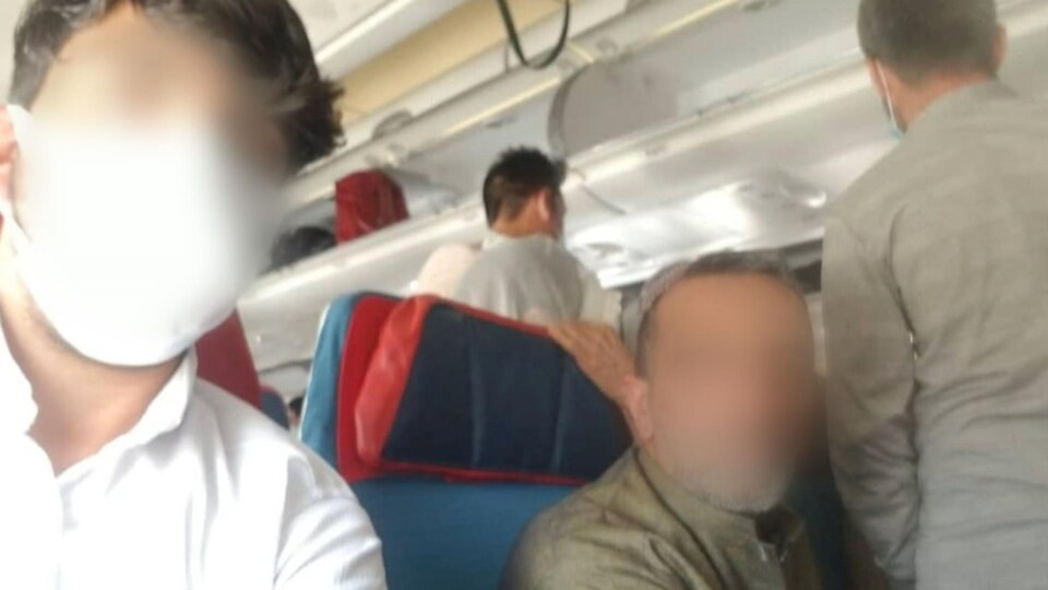 Les deux hommes, aux visages floutés, sont assis dans l'avion.