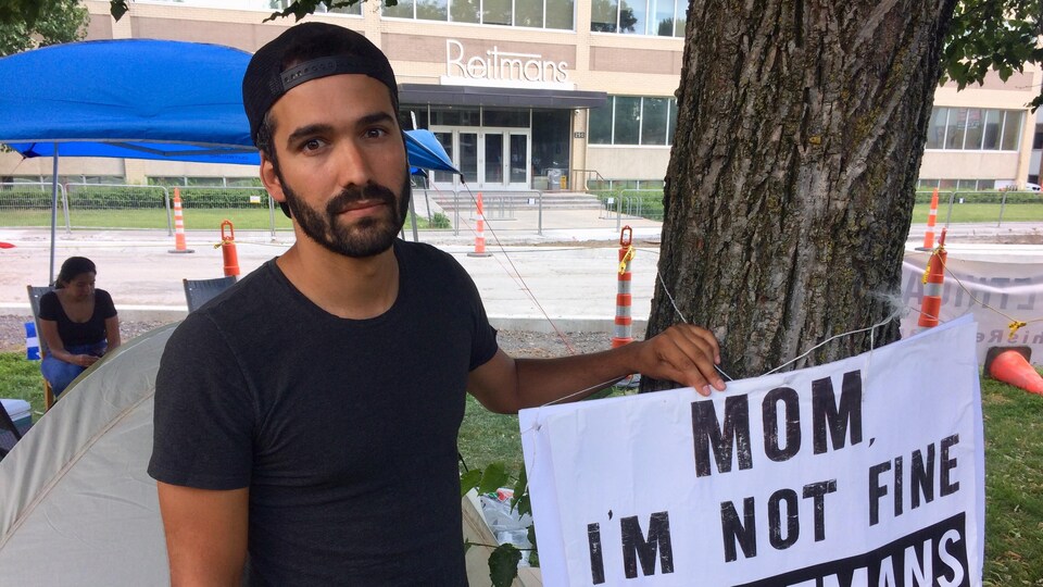 L'influenceur Kubben Quiñonez tient une pancarte où il est écrit « Mom I'm not fine because of Reitmans »