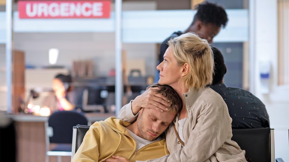 La femme et le jeune homme sont assis dans une salle d'attente, elle le tient dans ses bras.