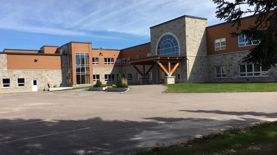 Le bâtiment est en pierre et en bois. Il y a un grand stationnement.