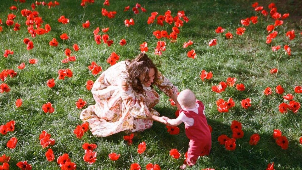 Au centre d'un champ de fleurs rouges, une femme souriante tient les mains d'un jeune enfant.