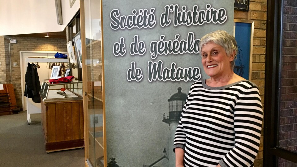 On voit Monique Fournier devant un panneau où il est écrit « Société d'histoire et de généalogie de Matane ».
