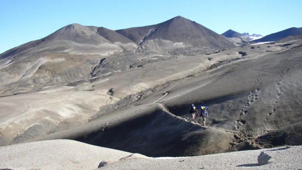 Deux personnes marchent avec leur sac à dos le long d'une montagne.