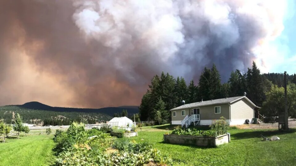Un panache de fumée s'élève de derrière une maison.