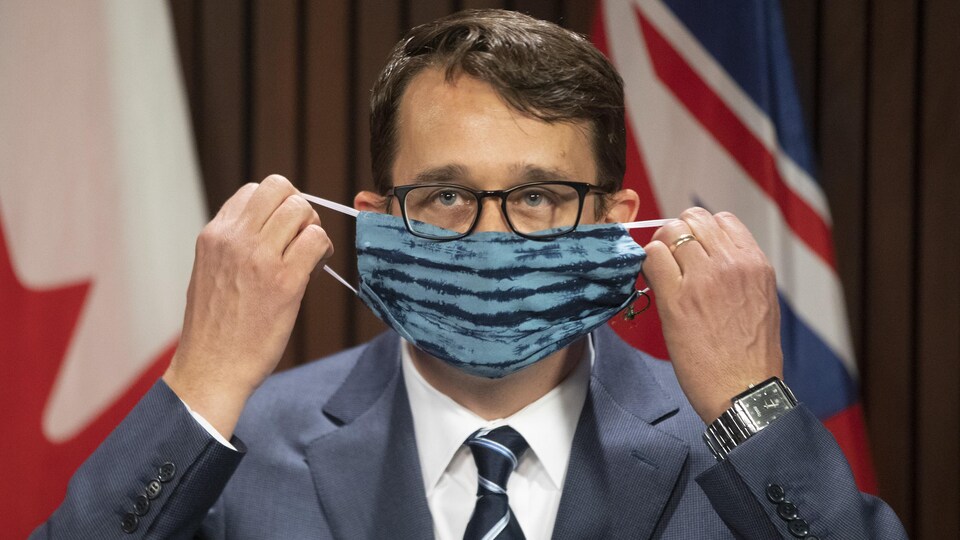 Le ministre Monte McNaughton, enlève son masque au cours d'une conférence de presse.