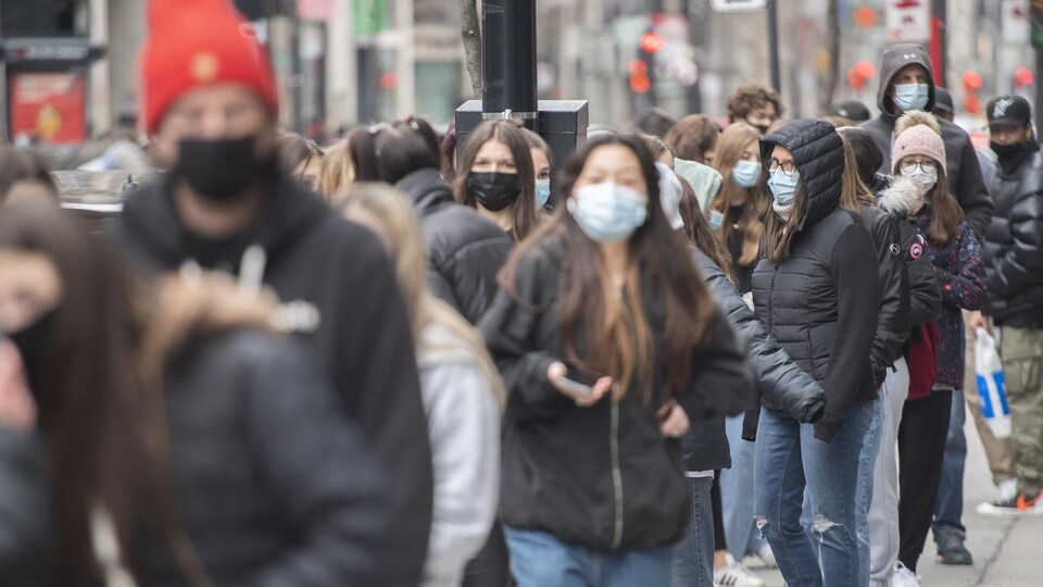 De jeunes gens font la file sur le trottoir en portant un masque.
