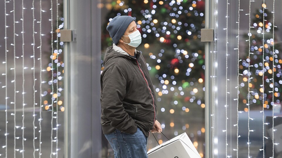 Un homme masqué marche devant un commerce illuminé.