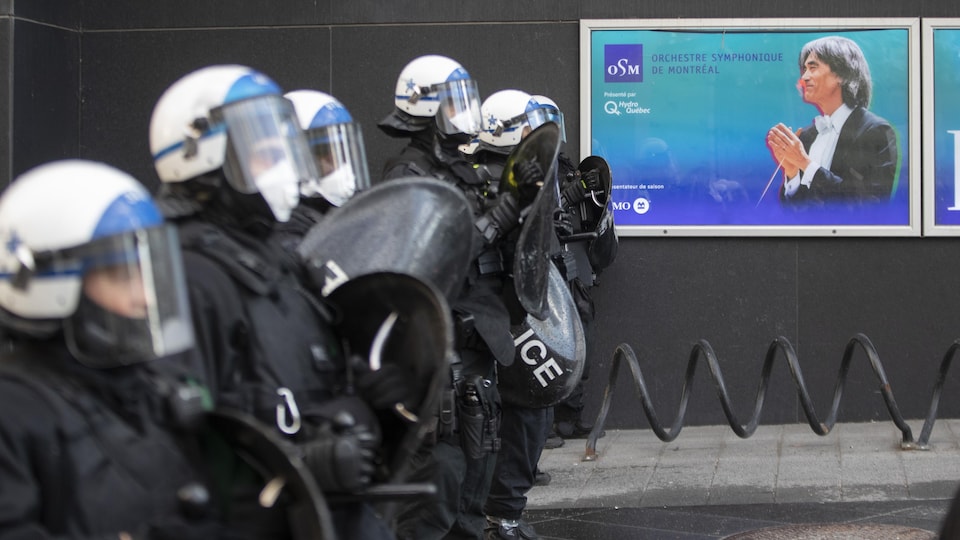 Un rang de policiers antiémeutes attend près d'une affiche de l'Orchestre symphonique de Montréal.