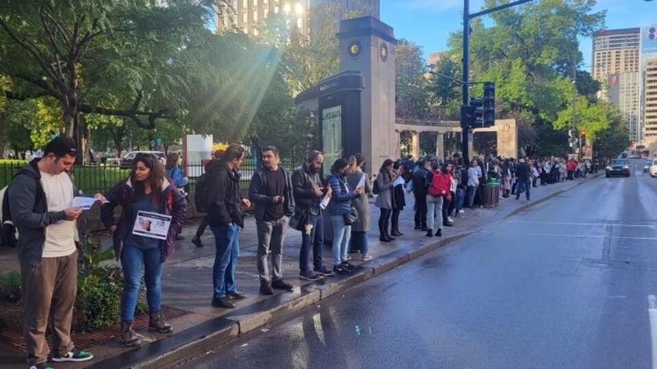 Des dizaines de personnes forment une chaîne humaine sur un trottoir de la rue Sherbrooke à Montréal.