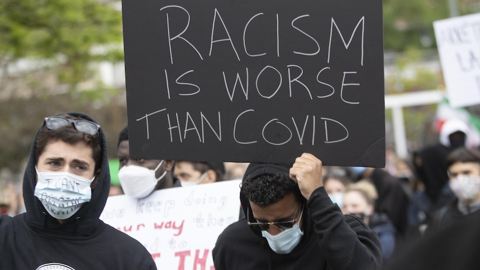 Un manifestante sostiene un cartel escrito en inglés que dice que el racismo es peor que el COVID.