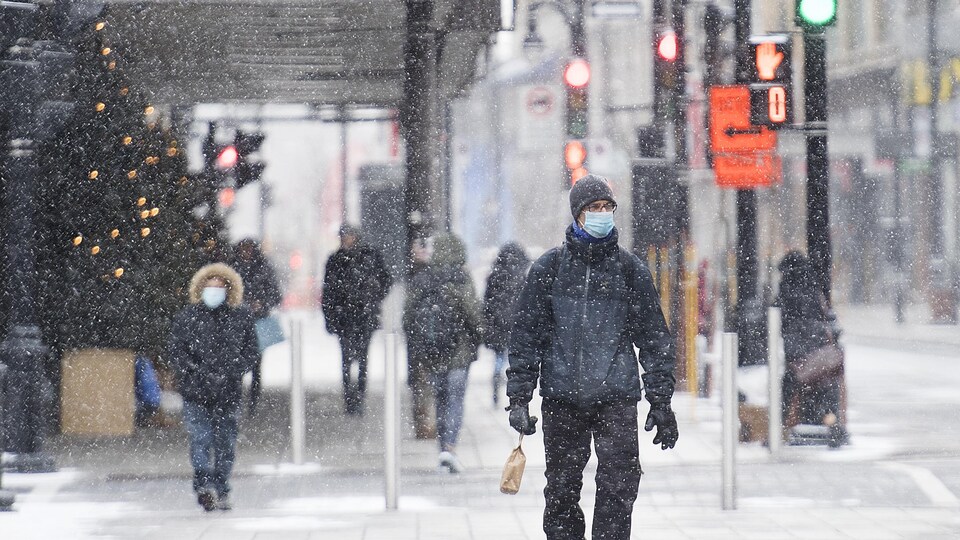 Des passants dans le centre-ville de Montréal sous une neige fine.