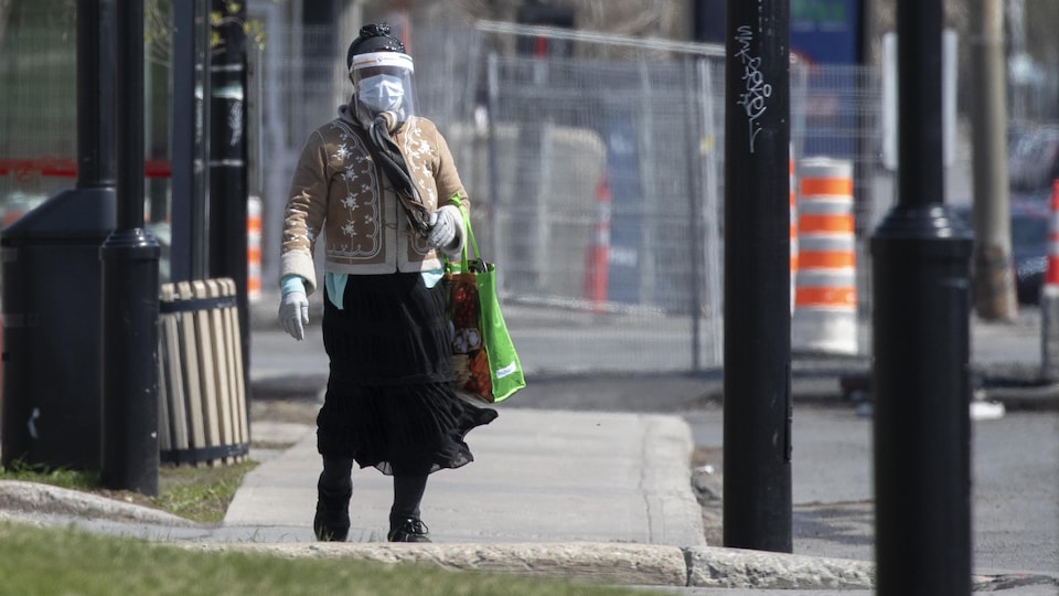 Une femme masquée marche sur un trottoir de l'arrondissement de Montréal-Nord.