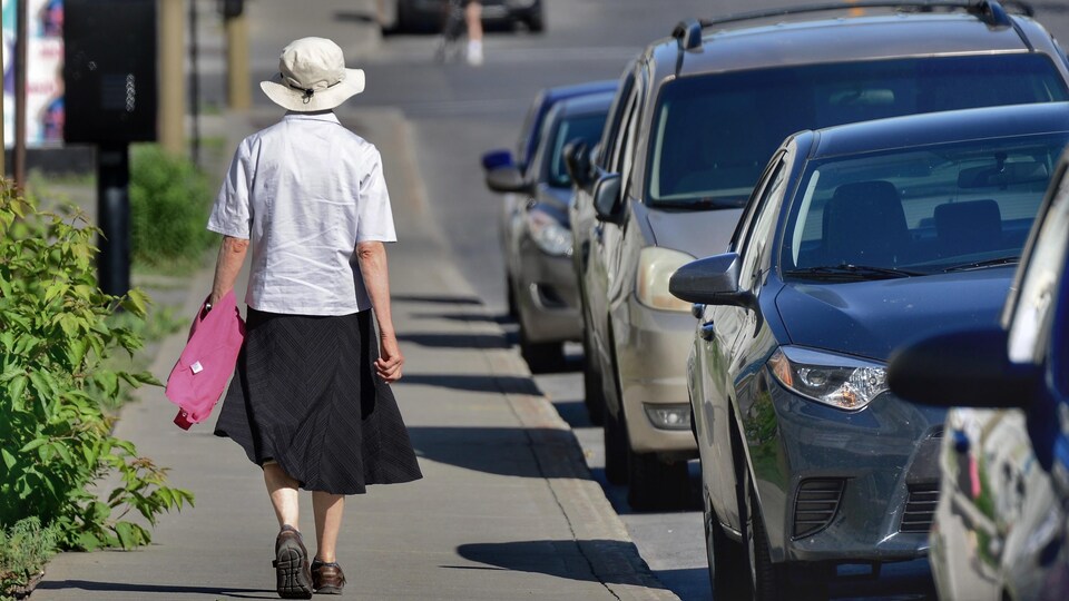Une femme âgée, qu'on voit de dos, marche sur un trottoir de Montréal.
