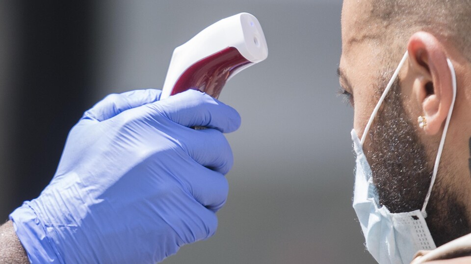 Une main gantée vise le visage d'un homme avec un thermomètre.