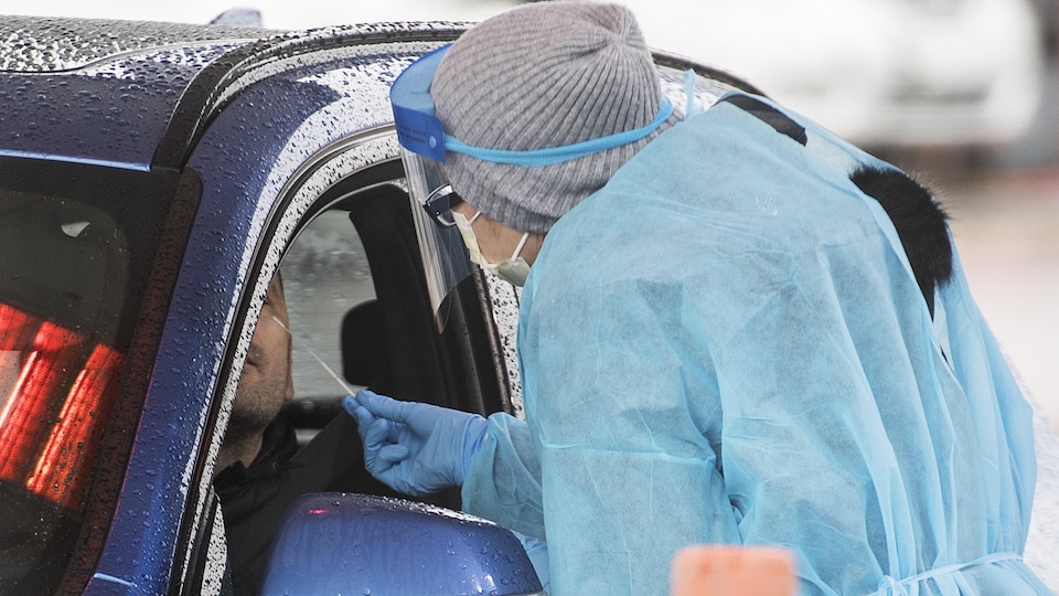 Une infirmière administre un test de la COVID-19 à une personne dans une voiture.