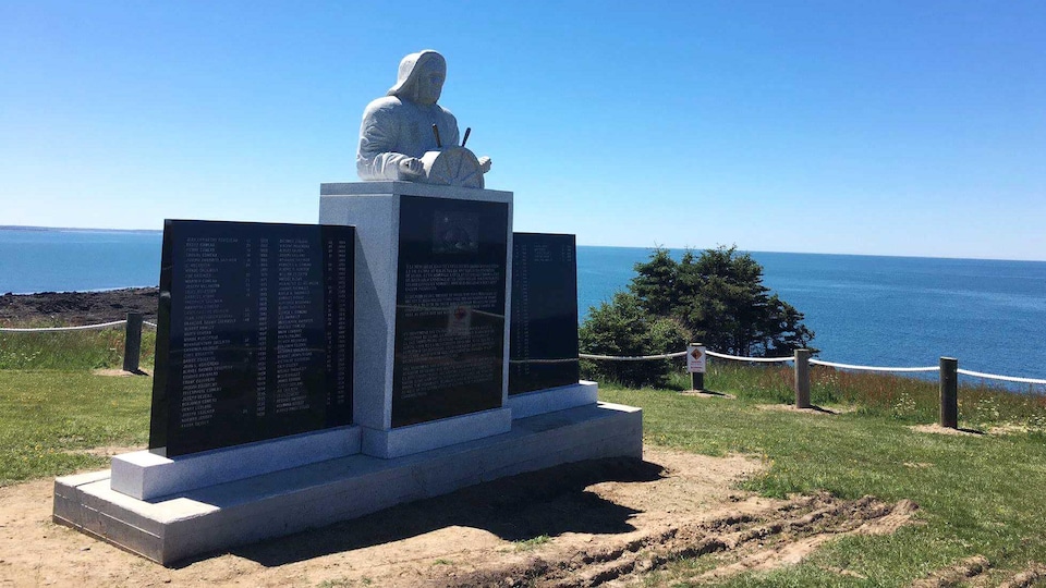 Gros plan sur le monument, sur une falaise, avec vue sur l'océan. Un capitaine de bateau tient la barre d'un navire au centre du monument. La sculpture est de l'artiste Marc Graff.