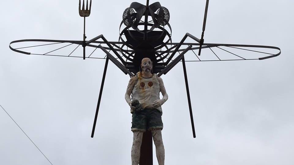 La sculpture d'un immense moustique avec des ustensiles qui transporte un homme.