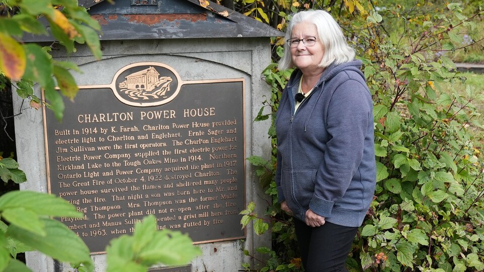 Une femme devant une plaque commémorative.
