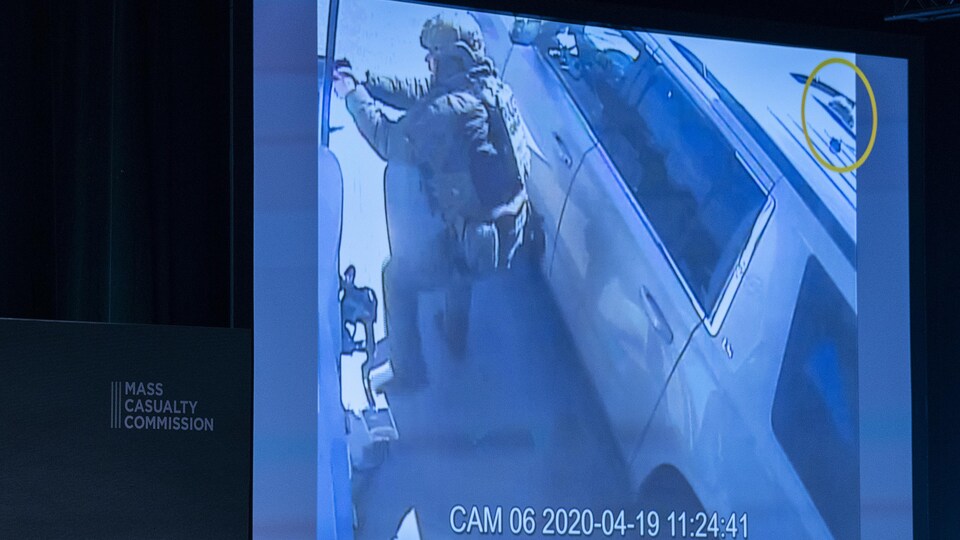 Sur un écran, on voit des images captées par une caméra de surveillance. Un policier en uniforme de l'escouade tactique est vu de profil en train de pointer son arme à feu.
