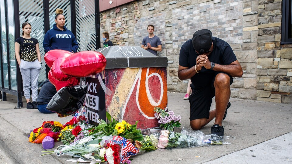Un homme à genoux fait une prière près du mémorial, sur lequel on peut lire : « Black Lives Matter » (La vie des Noirs compte).