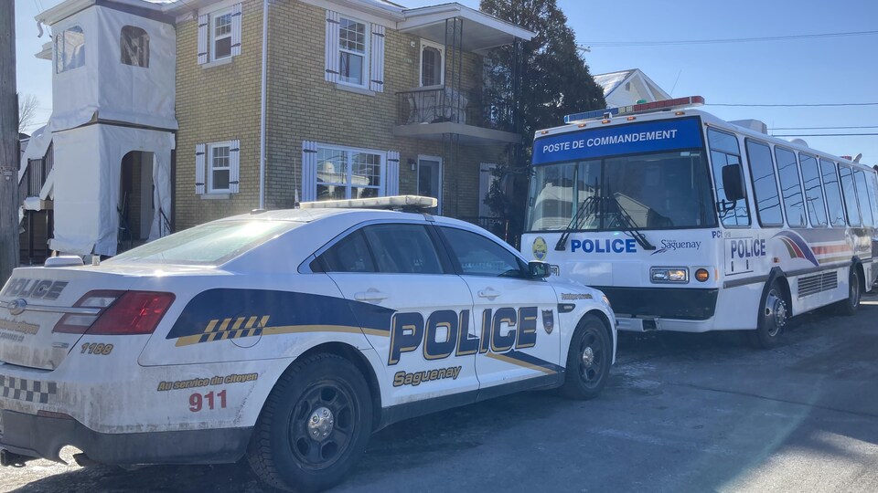 Une voiture du Service de police de Saguenay et le poste de commandement mobile stationnés devant une résidence.