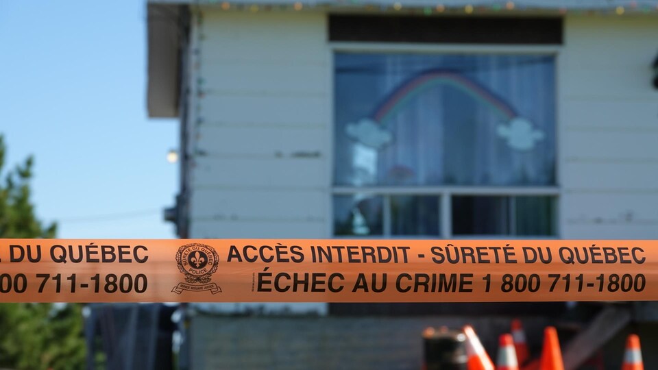 Un ruban orange de la Sûreté du Québec indiquant Accès interdit devant une maison.