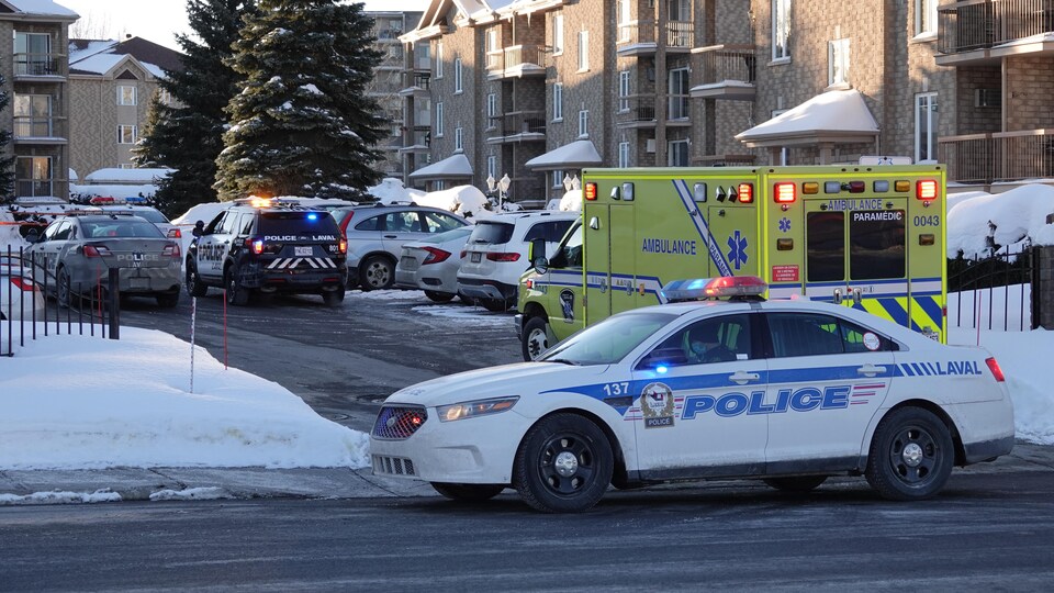 Une ambulance et des voitures de police sont stationnées devant l'immeuble.