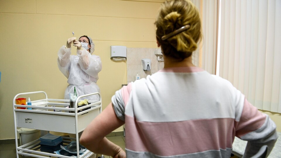 Une infirmière avec une dose de vaccin et une patiente, de dos, au premier plan.