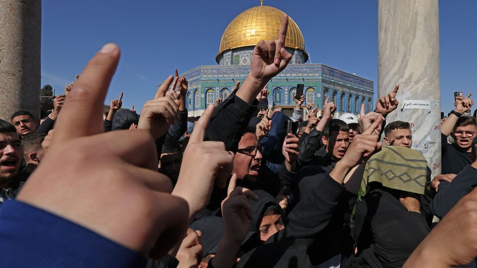 Des manifestants réunis sur l'esplanade de la mosquée lèvent les bras dans les airs.