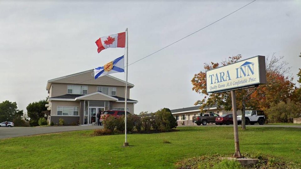 Le motel vu de la route. Des drapeaux du Canada et de la Nouvelle-Écosse flottent sur des mâts et une enseigne indique qu'il s'appelle « Tara Inn ».