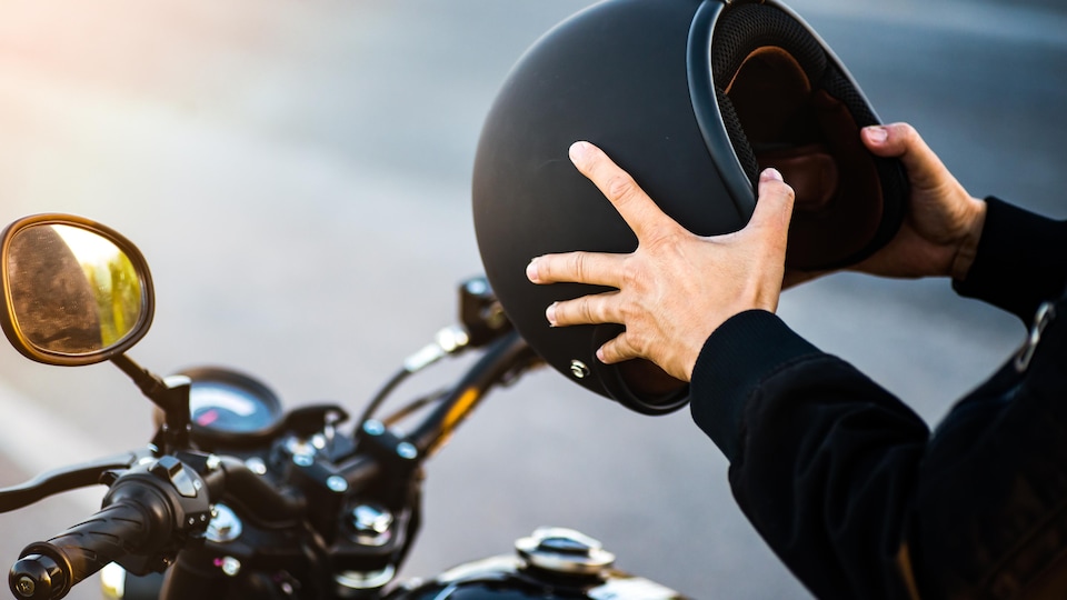 Un homme est assis sur une moto mais on voit seulement ses deux bras. Il tient un casque de moto comme s'il s'apprêtait à le mettre sur sa tête.