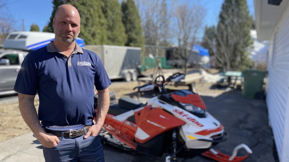 A man posed in front of his snowmobile.