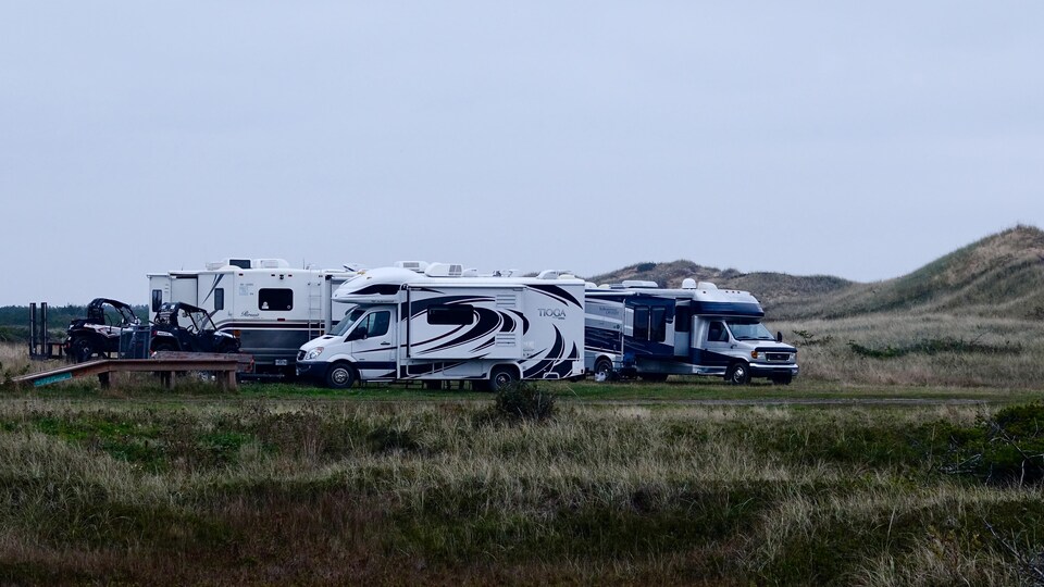 Des motorisés de camping et des quads sont stationnés près des dunes.