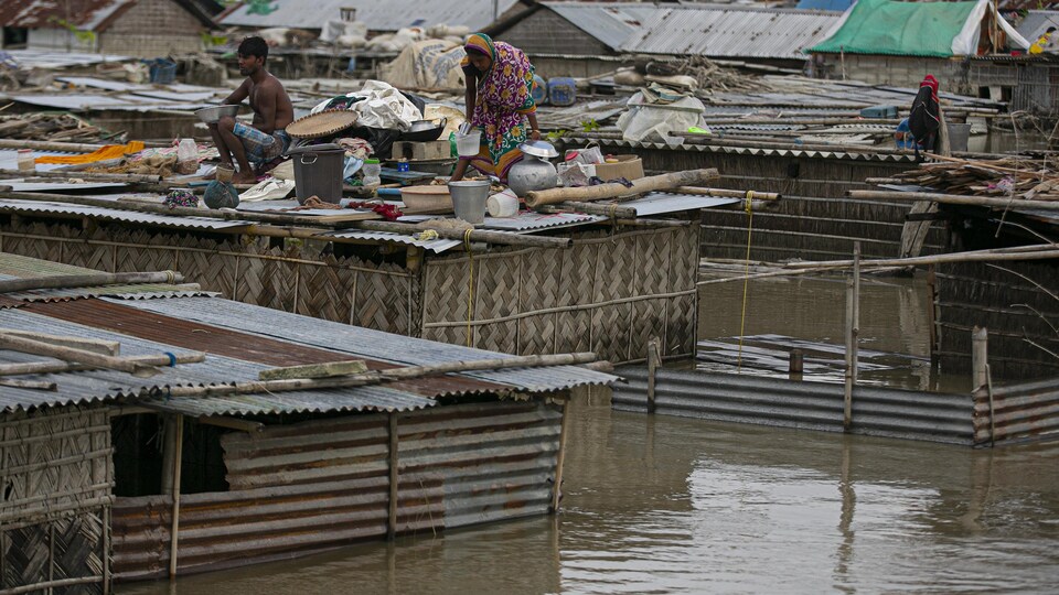 Des gens sont réfugiés sur le toit plat de leur demeure pour échapper à l'eau boueuse. 