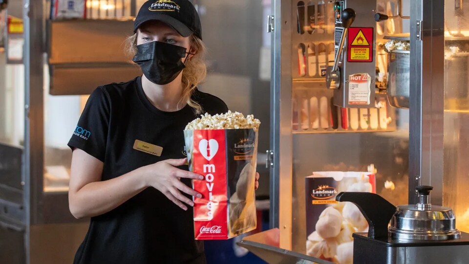 Une personne portant un max sur le visage et un sac de maïs soufflé dans les mains.
