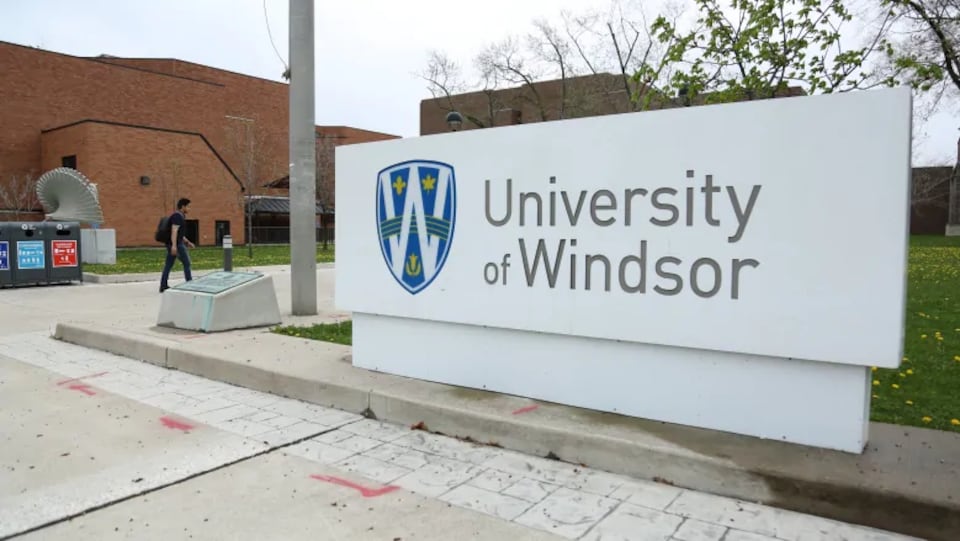 Un panneau de l'Université de Windsor avec un étudiant qui marche au loin.