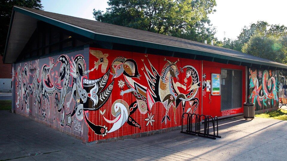 Peinte sur un chalet de parc, la murale représente des formes inconnues sur un fond rouge.