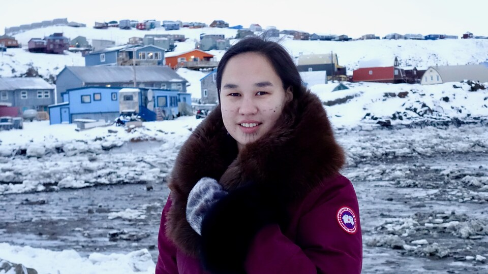 Mumilaaq Qaqqaq porte un manteau rouge. En arrière-plan, la capitale du Nunavut, Iqaluit.