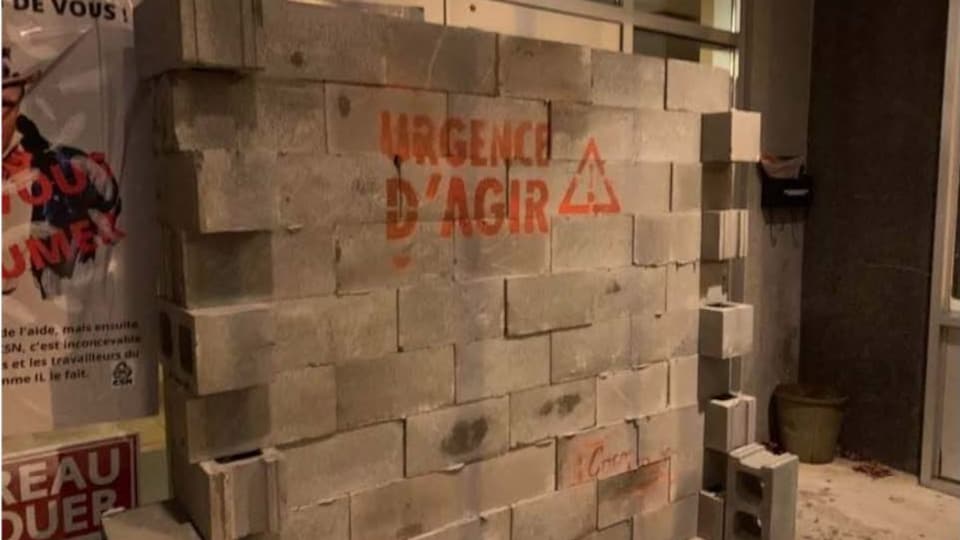 Un mur de briques devant une portes sur lequel on peut lire : "Urgence d'agir!".
